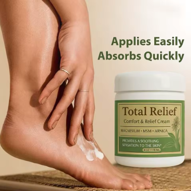 A close-up lifestyle shot of a person massaging Total Relief Cream onto their foot and lower leg, featuring the text overlay 'Applies Easily Absorbs Quickly' to demonstrate the application of magnesium and arnica for tired and restless legs."